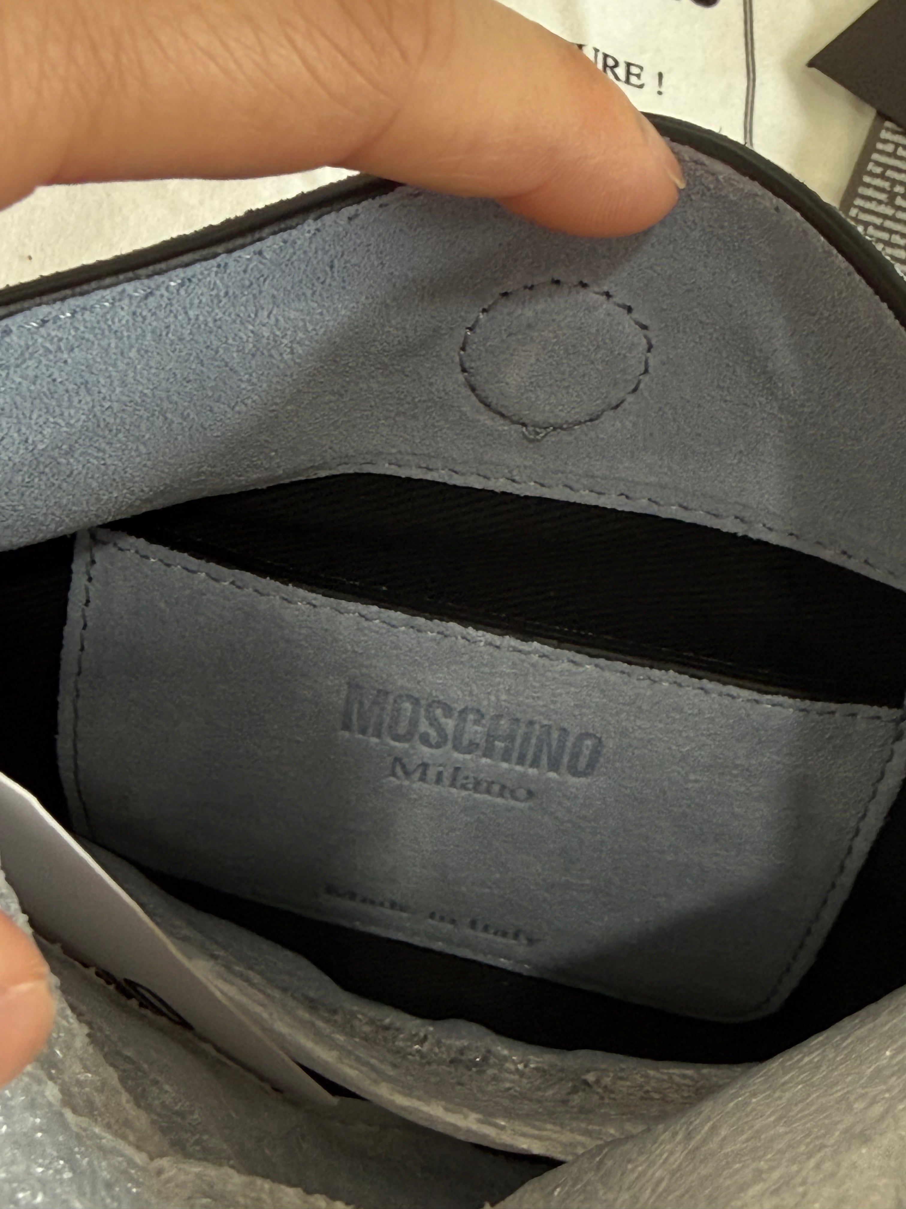 Close-up of a Moschino pouch with a hand holding it open.